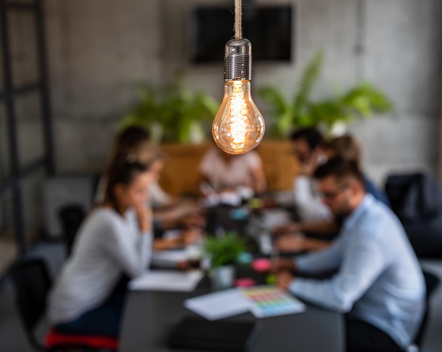 A light bulb in front of workers around a conference table